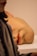 A large, realistic sculpture of a portion of a human face lays on its side on a flat surface. Details, including skin texture and facial stubble, are meticulously crafted. In the foreground, part of a person's face and shoulder is visible, slightly out of focus.