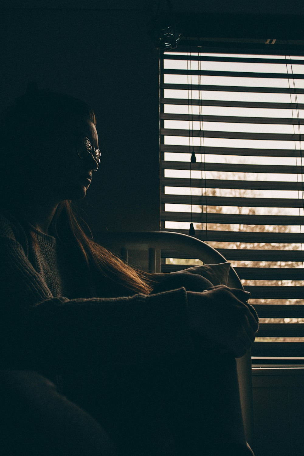 woman sitting on bed beside window with blinds