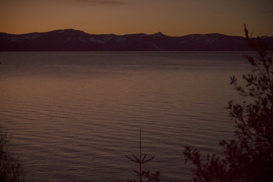 A minimalist landscape at dusk with gentle shadows stretching across a calm lake.