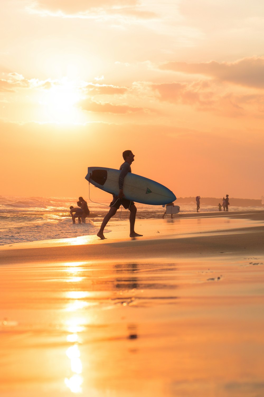 hombre sosteniendo la tabla de surf durante la puesta del sol