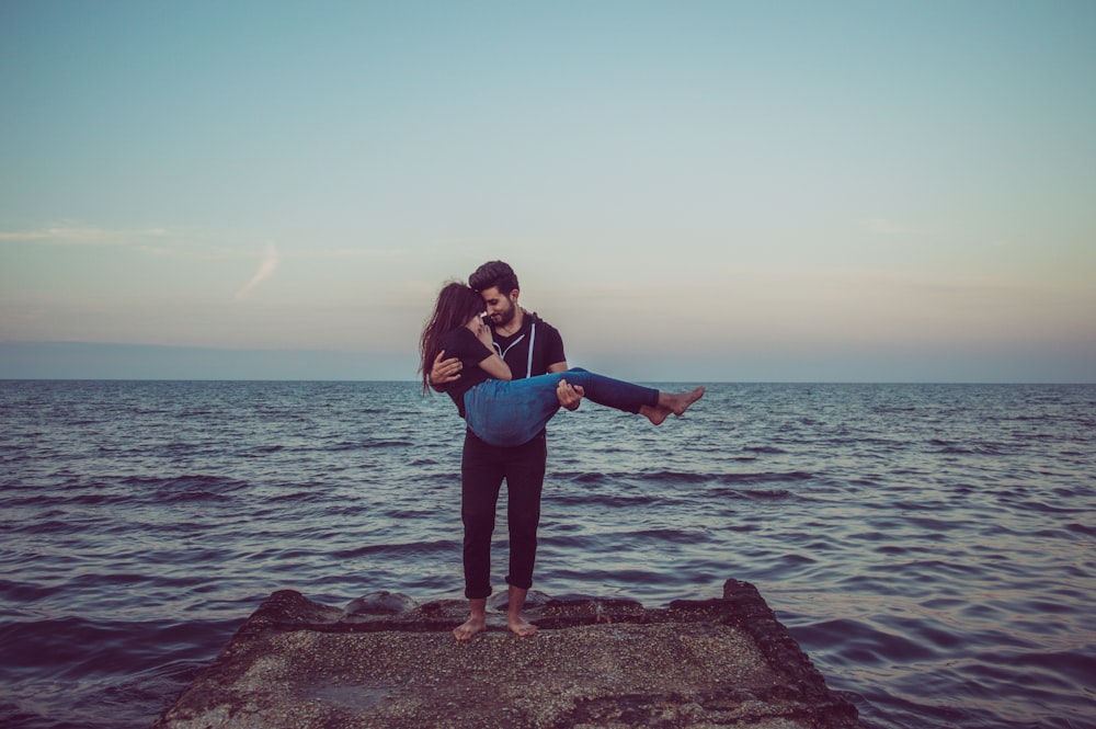 man carrying woman by a concrete sea dock