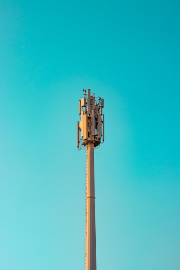 Technician inspecting a tall antenna support structure against a clear blue sky.