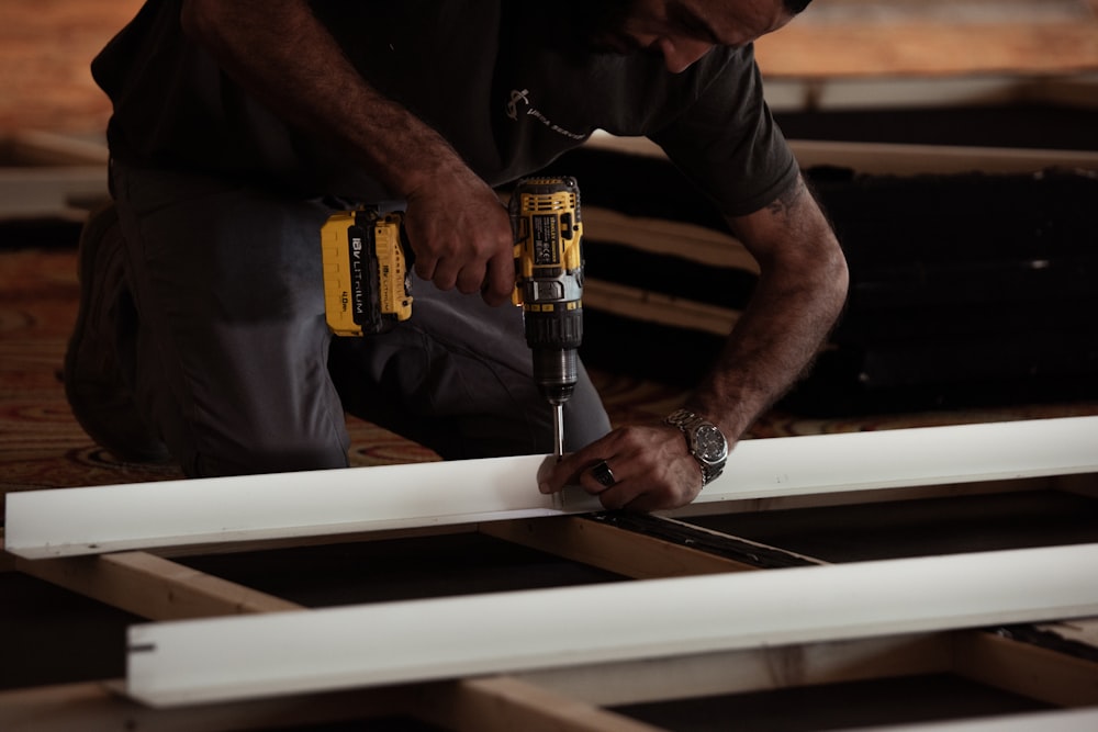 homme perçant sur une planche de bois à l’aide d’une perceuse électrique