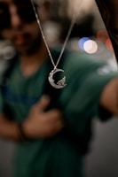 Close-up of a delicate silver necklace featuring a crescent moon pendant shimmering under soft light.