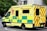 A large, yellow and green emergency ambulance is parked on a city street. The vehicle is part of the London Ambulance Service, as indicated by the text and logos on its side. It features red and yellow chevron patterns on the back doors and displays several identification numbers and emergency contact information.