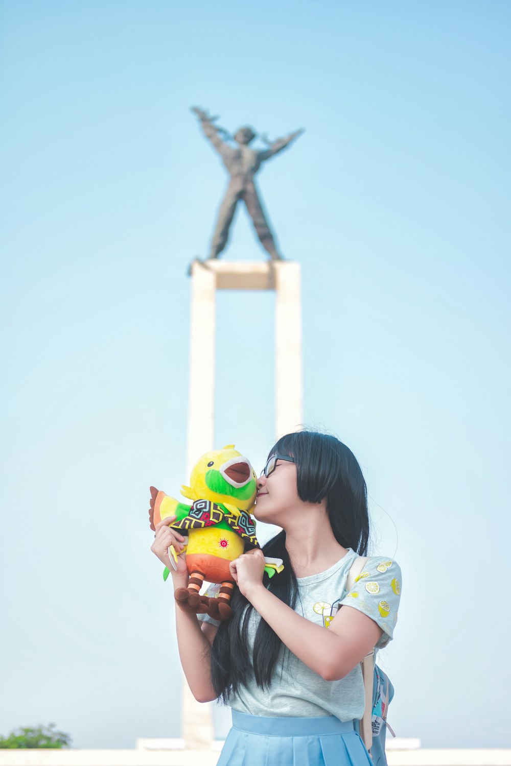 girl kisses yellow bird plush toy near monument