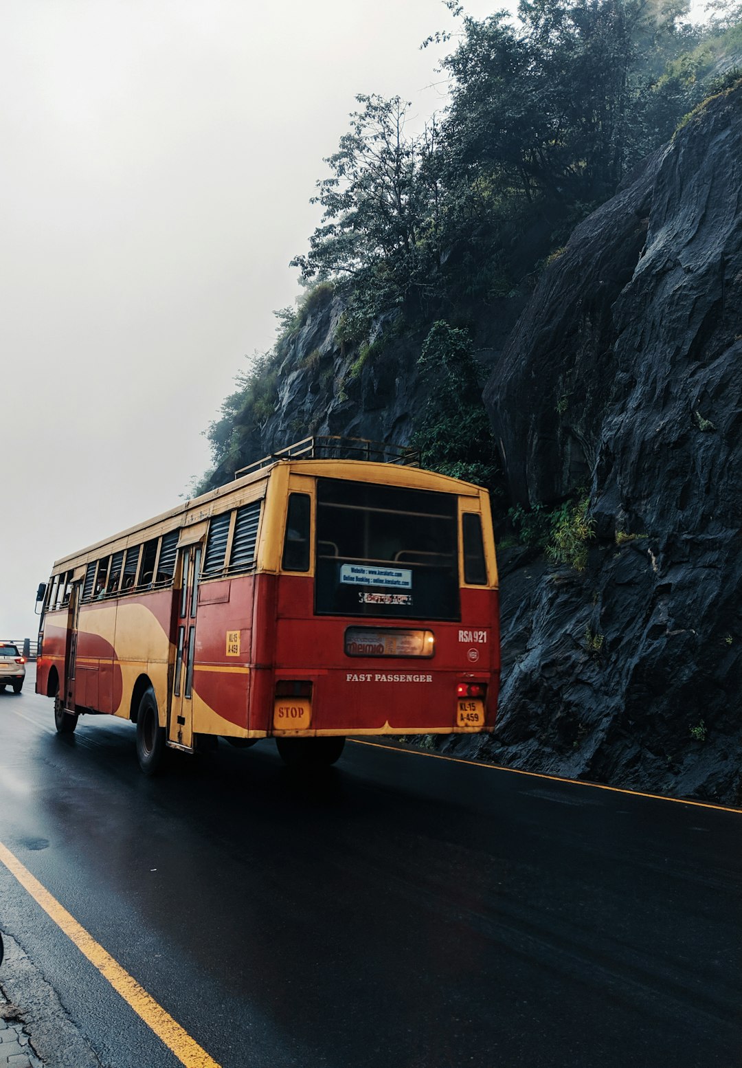 yellow and red bus passing by a wet road