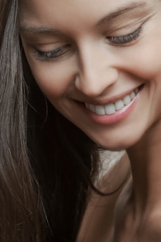 A soft, warm close-up of a woman smiling gently, eyes sparkling with quiet confidence.