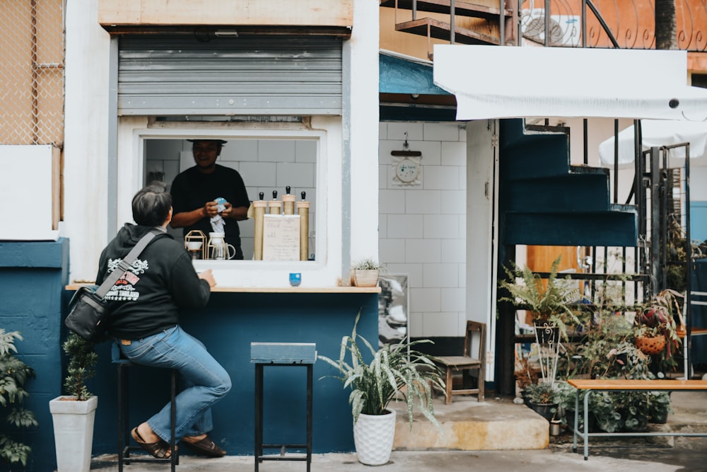 man sits beside open store