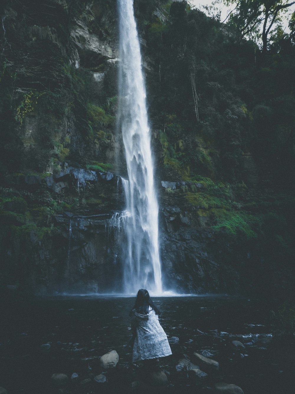 girl on rocky shore facing the waterfalls