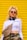 A person with long blonde hair tied up in a high ponytail wears sunglasses and large earrings. They are dressed in a white long-sleeve crop top with the word 'MIAMI' on it, camo pants, a crossbody bag with a brown and beige pattern, and headphones around their neck. A yellow shutter serves as the background.