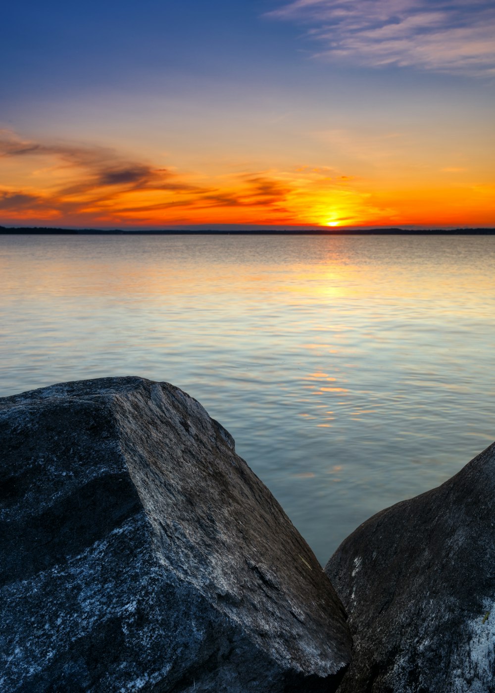 Die Sonne geht über dem Wasser unter, mit Felsen im Vordergrund