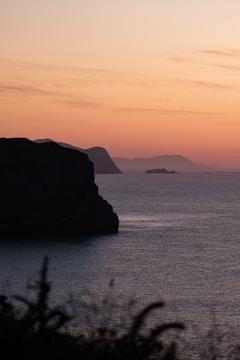 A panoramic view of a large-scale art piece on a coastal cliff during sunset.