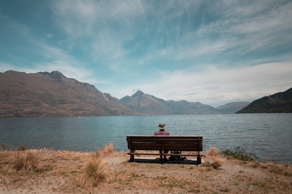 person sitting on wooden bench front of the sea