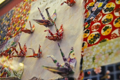 Colorful origami cranes arranged in a dynamic pattern against a backdrop of intricately patterned paper, highlighting a mix of traditional Japanese designs.