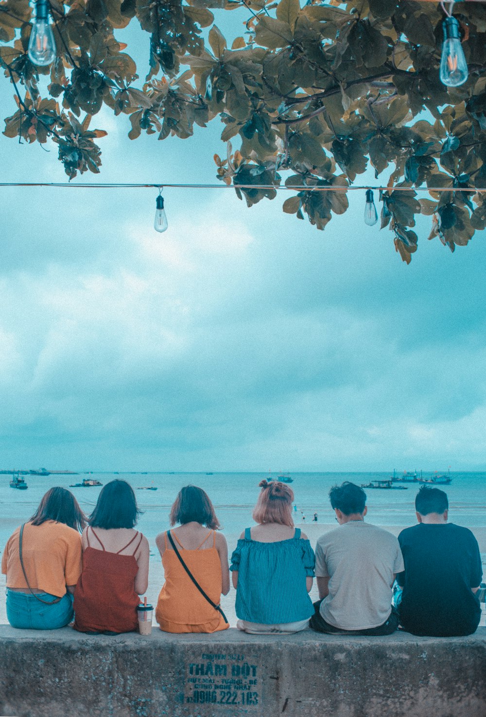 six people sitting and facing near blue sea under blue and white skies during daytime