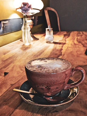 A cozy café table with a steaming cup of coffee, a fresh croissant, and a small vase with flowers.