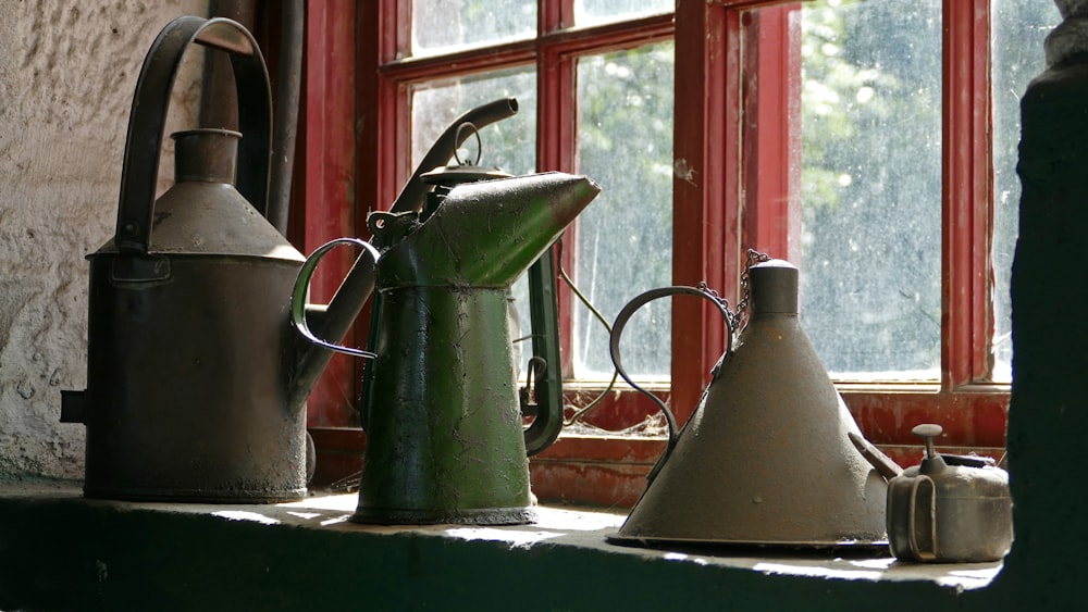 vintage four watering cans by window during daytime