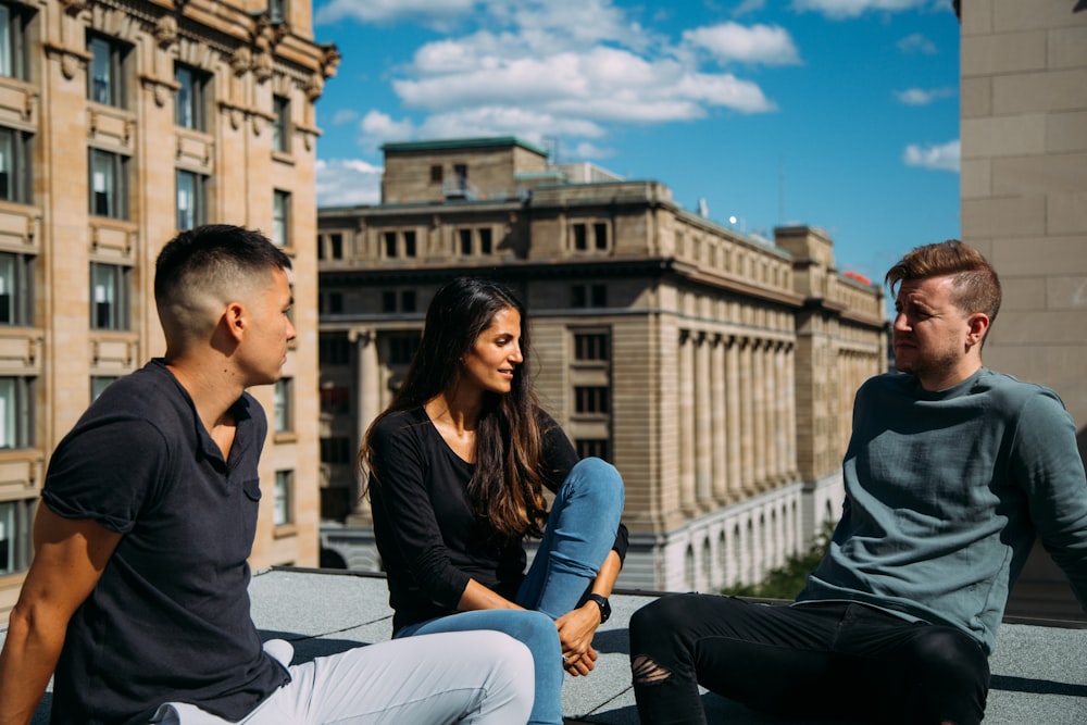 woman sitting between two men on a building rooftop