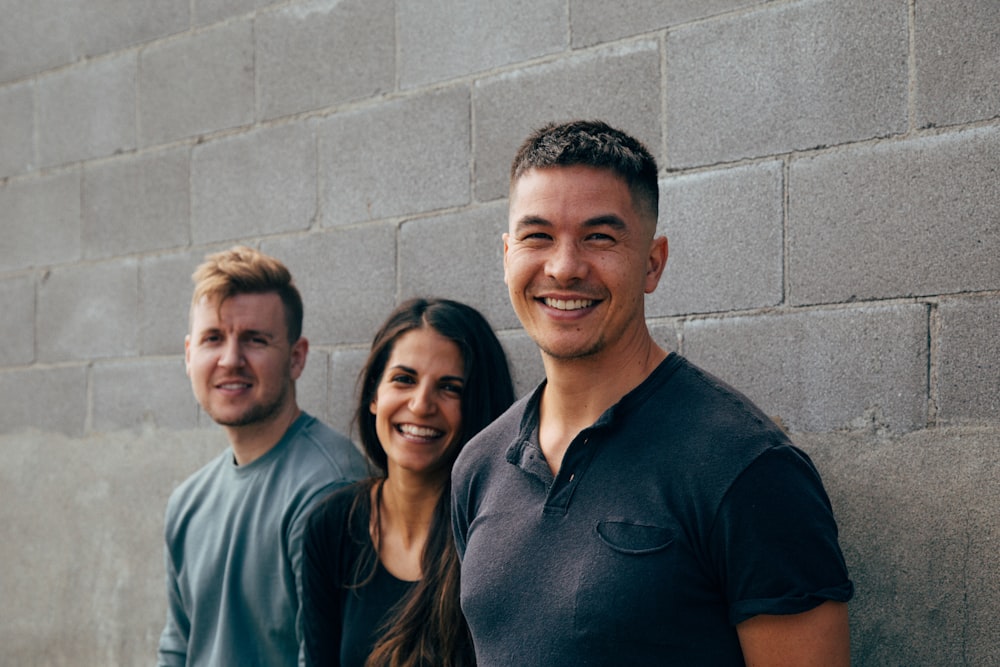 dos hombres y una mujer sonriendo apoyados en la pared