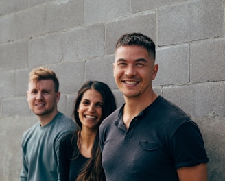 two men and woman smiling leaning on wall