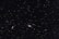 A vast, star-filled sky with countless stars scattered across the dark expanse. Two prominent galaxies are visible: a spiral galaxy with a bright core and extended arms on the right, and a smaller, elongated galaxy on the left.