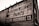A brick wall displays a large vintage advertisement for Sherwin-Williams Paints and Helena Hardware Co. The painted sign is weathered, showing signs of age and wear, giving it an antique appearance. The text is bold and prominently positioned, with an iconic paint can logo visible on the left.