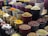 A vibrant display of various spices and herbs arranged in multiple large bowls. The containers are filled with colorful ingredients, such as dried peppers, turmeric, and other spices, creating a visually appealing and aromatic market scene.