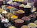 A vibrant display of various spices and herbs arranged in multiple large bowls. The containers are filled with colorful ingredients, such as dried peppers, turmeric, and other spices, creating a visually appealing and aromatic market scene.