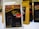 A package of Aman Kuba Luwak coffee is prominently displayed in the foreground, featuring a graphic of coffee beans and gold text on a black background. Other similar coffee packages are arranged in the background, slightly blurred.