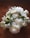 A bouquet of white flowers, including roses, tulips, and peonies, resting on a wooden surface. The flowers are fresh and lush, with green leaves interspersed among the blossoms, creating a natural and elegant arrangement.