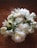 A bouquet of white flowers, including roses, tulips, and peonies, resting on a wooden surface. The flowers are fresh and lush, with green leaves interspersed among the blossoms, creating a natural and elegant arrangement.
