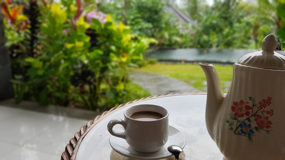 coffee in white ceramic teacup near white and multicolored teapot on round table