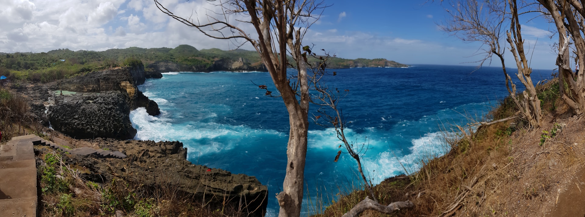 A panoramic shot of the rugged coastline where the forest meets the sea, capturing waves crashing against rocky shores at Ujungkulon.