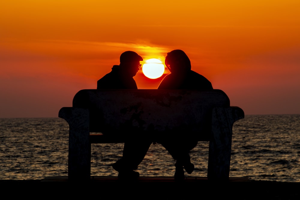 silhouette of man and woman sitting on bench while facing each other