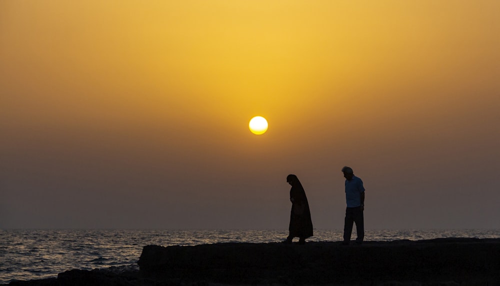 silhouette of man and woman by the body of water at sunset