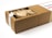 A rectangular cardboard box partially opened to reveal its contents, which include multiple paper-wrapped items. The box features a white label on top with text and a small design element.
