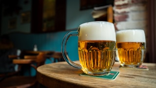 beer in clear glass mugs on round brown wooden table