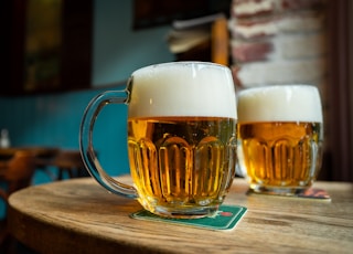 beer in clear glass mugs on round brown wooden table