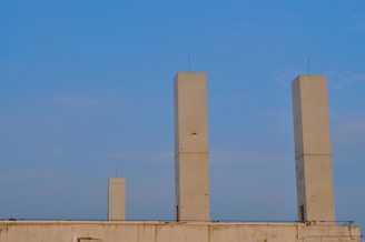 Three tall, rectangular beige towers stand on a rooftop with a clear blue sky in the background. The structures are evenly spaced and feature small antennas on top.