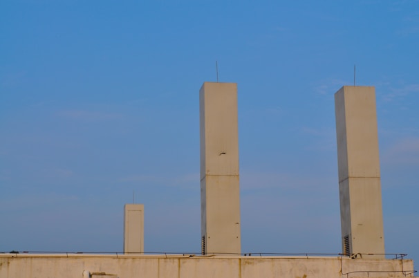 Three tall, rectangular beige towers stand on a rooftop with a clear blue sky in the background. The structures are evenly spaced and feature small antennas on top.