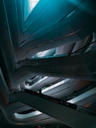 A modern interior featuring abstract, sweeping architectural lines that form a multi-level structure. The lighting is subtle, casting soft shadows and highlights across the sleek surfaces. An escalator can be seen with a few silhouetted figures standing on it, adding a sense of scale and movement.