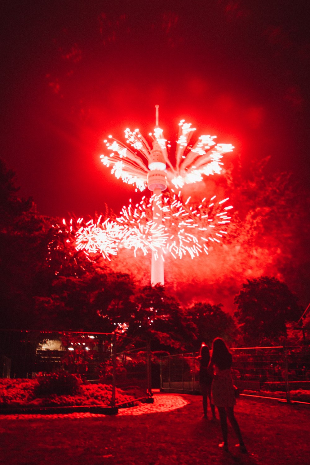 Dos personas de pie frente a fuegos artificiales rojos