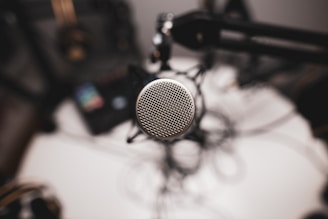 A close-up of a microphone with a blurred podcast studio background in grayscale.