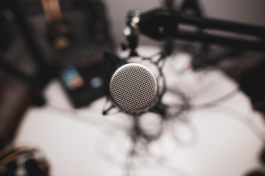 A close-up view of a microphone, with a metal mesh grille, is mounted on a boom arm. The background is blurred, adding depth to the image. Other podcasting or recording equipment is subtly visible, adding context to a studio setting.