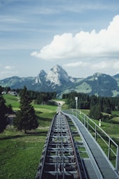 aerial photography of train railway near green field viewing mountain under white and blue skies during daytime