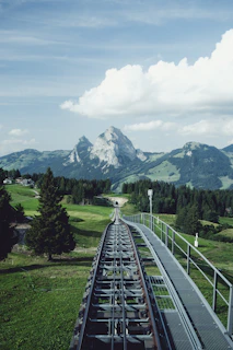 aerial photography of train railway near green field viewing mountain under white and blue skies during daytime