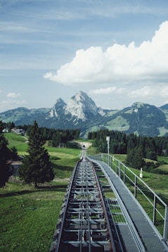 aerial photography of train railway near green field viewing mountain under white and blue skies during daytime