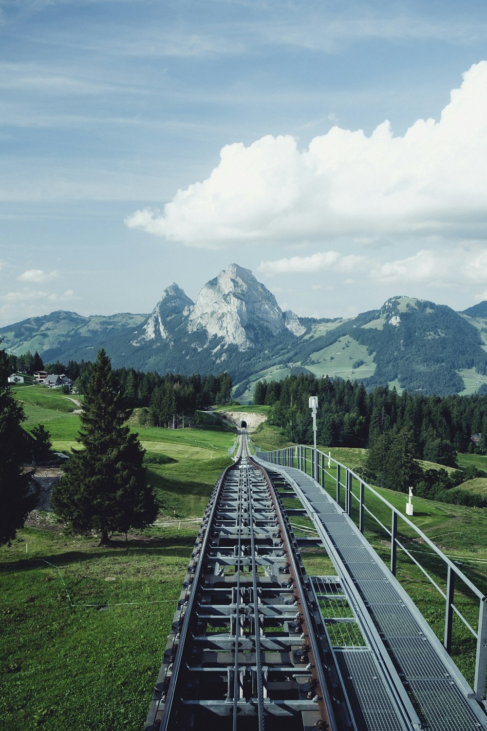 Luftaufnahme der Eisenbahn in der Nähe der grünen Wiese mit Blick auf den Berg unter weißem und blauem Himmel während des Tages