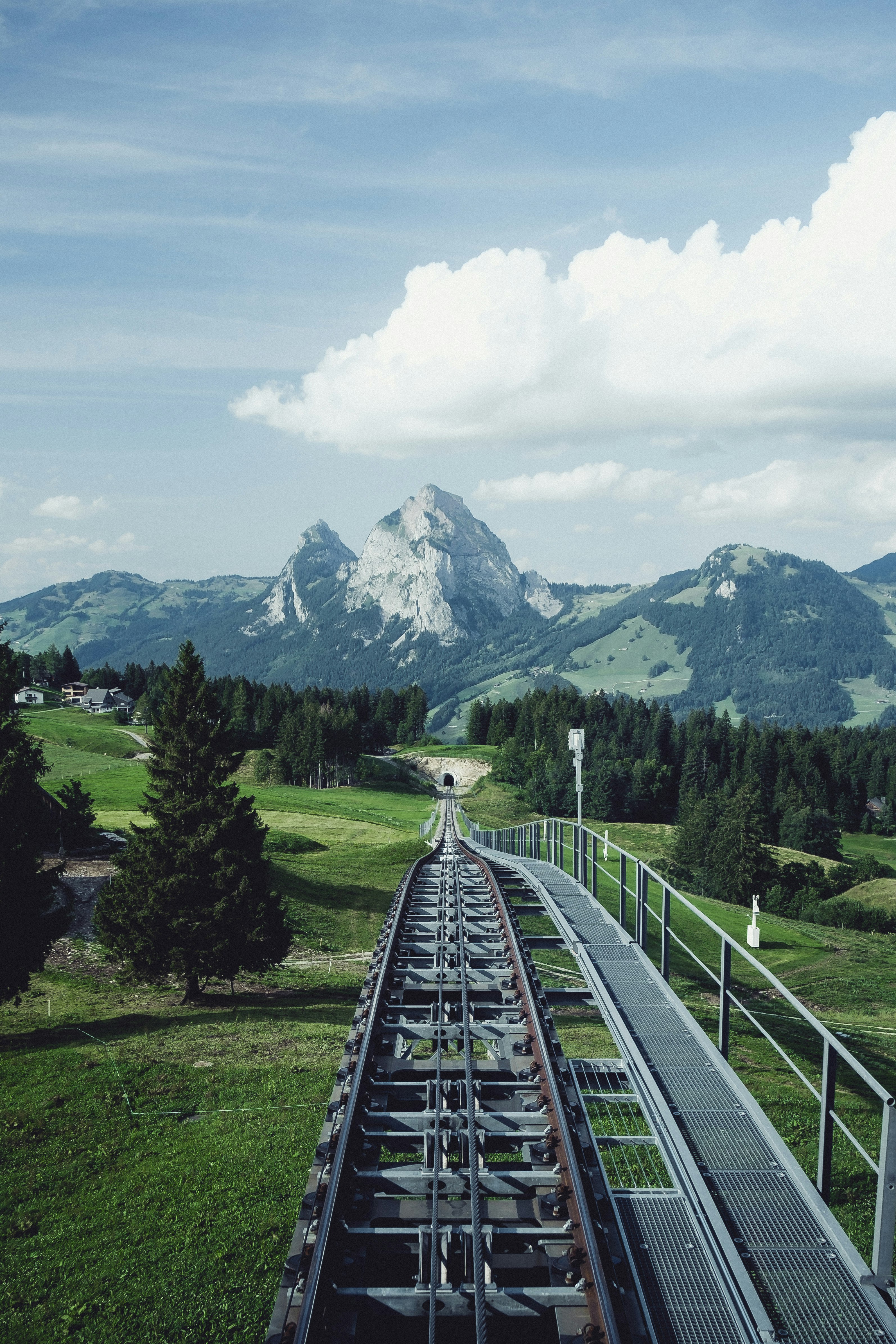 aerial photography of train railway near green field viewing mountain under white and blue skies during daytime